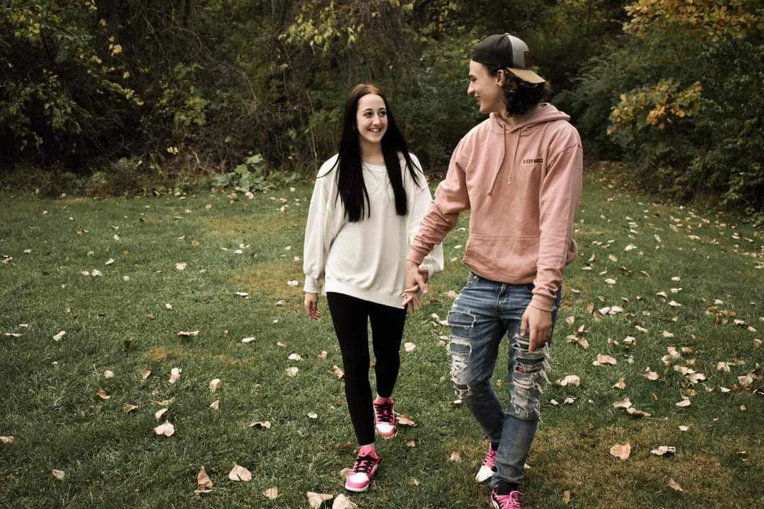 Young couple walking hand-in-hand on leaf-scattered grass in autumn