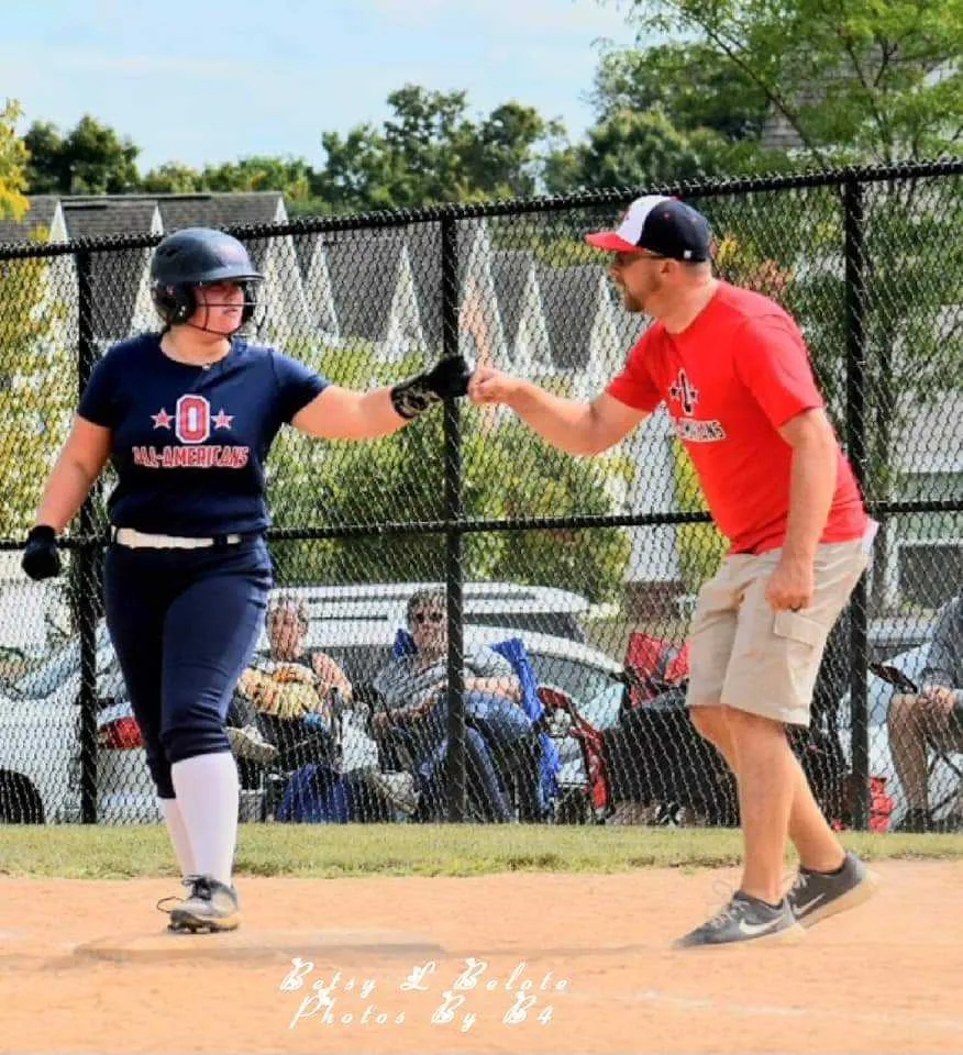 Youth softball player fist-bumps base coach near third base during game